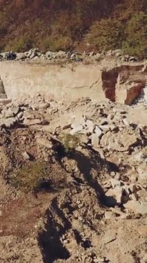 Profesyonel ekipmanlı işçiler kumlu taş ocağında büyük taşların arkasında ve ağaçlı bir tepede çalışıyorlar. Kamera hareketi yukarı. Dikey video