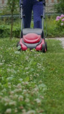 Bahçesinde çim biçen kadın elektrikli çim biçme makinesiyle dikey video çekiyor.