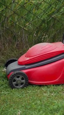 Bahçede çim biçme makinesiyle çim biçen çıplak ayaklı genç bir kız. Çıplak kadın ayakları arka bahçede çim biçme makinesinin arkasında yürüyor. Dikey video