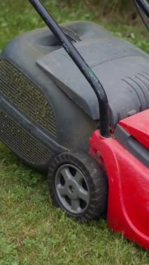 Çim biçme makinesiyle taze yeşil çimleri biçiyorum. Bahçede çim biçme makinesiyle çim biçen çıplak ayaklı genç bir kız. Dikey video