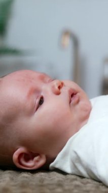 Sevimli erkek bebek sırt üstü yatıyor. Beyaz tişört giyen yenidoğan ellerini sallıyor ve yukarı bakıyor. Kapatın. Dikey video