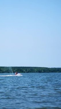 Güneşli bir günde nehirde jet ski bisikleti süren insanlar. İki su motorcusu yavaşça rıhtıma yaklaşıyor. Dikey video