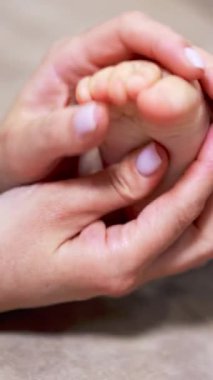 Annemin elleri bebek ayağını tutuyor ve okşuyor. Annem oğluyla evde vakit geçiriyor. Kapatın. Arkaplan bulanık. Dikey video