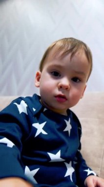 Kameraya dokunmaya çalışan tuhaf beyaz bir çocuk. Çocuk bir kenara çekilip telefonda dikkatini dağıtıyor. Düşük açı. Dikey video