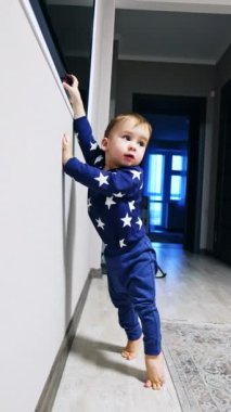 Kafkasyalı çocuk parmaklarının üzerinde durup duvardaki televizyona ulaşmaya çalışıyor. Bebek televizyonu açmaya çalışıyor. Dikey video