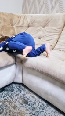 Mutlu küçük bebek kanepeye neşeyle tırmanıyor. Sevimli aktif çocuk salonda tatlı tatlı gülümsüyor. Dikey video