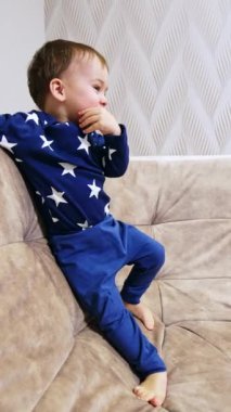 Kafkasyalı mutlu çocuk arkaya yaslanmış büyük kanepenin üzerinde duruyor. Sevimli bebek el çırparak gülüyor. Dikey video