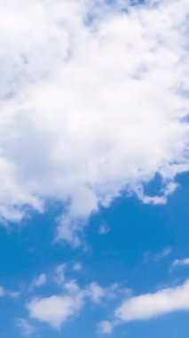 Açık mavi gökyüzünde beyaz bulutları dönüştürüyor. Düşük açılı görüşten yaz gökyüzü. Zaman ayarlı. Dikey video