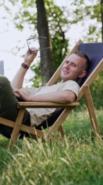 Adam işe ara verdi ve katlanır sandalyeye uzandı. Freelancer dizüstü bilgisayarı tutuyor ve bir kenara bakıyor, fikir arıyor. Dikey video