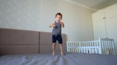 Aktif çocuk ayakları üzerinde durur ve zıplamaya başlar. Yatak odasında eğlenen neşeli çocuğa düşük açılı bakış açısı.