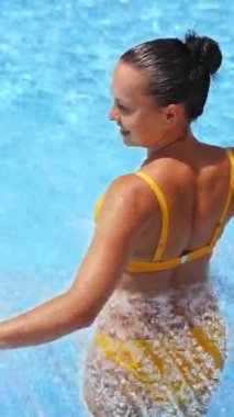 Yaz günü havuzda mutlu bir kadın. Yüzme havuzunda suyun keyfini çıkaran genç bir kadının arka görüntüsü. Dikey video