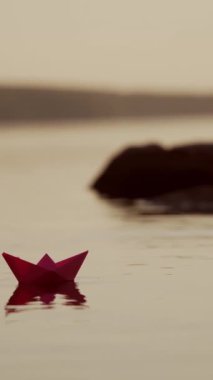 Kadının eli nehirde kırmızı ve yeşil kağıt gemileri fırlatıyor. Origami Kağıt Tekneleri gölde yüzüyor. Güzel Dalgalar Dalgalanma Arkaplanı. Seyahat ve doğa kavramı. Filtrelenmiş video. Dikey video