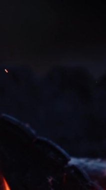 Çakıp çakıp ateş çıkaranlara, Kırmızı ve turuncu alev yükseliyor. Karanlık arka planda yanan siyah kütükler. Ağır çekim. Dikey video