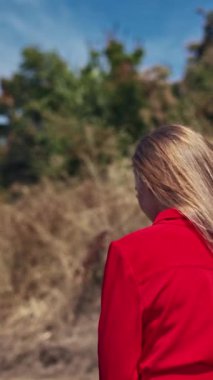 Uzun saçlı, seksi bir kadındı. Doğada yürüyen parlak elbiseli güzel bir kadının arka görünüşü. Ağır çekim. Dikey video