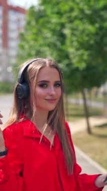 Güzel bir kız. Kulaklıklı genç bir kadının portresi. Güzel bir kadın, şehir gökdelenlerinde kulaklıkla müzik dinliyor. Dikey video