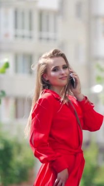 Şehirde inanılmaz bir kadın var. Cep telefonuyla konuşan genç ve güzel bir kadının portresi. Yazın açık havada kırmızı elbiseli, güzel, güler yüzlü bayan. Dikey video