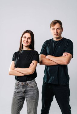 İçeride kendine güvenen genç profesyoneller. İki birey güven içinde kollarını kavuşturmuş, bir stüdyo ortamında tarafsız bir arkaplana gülümsüyor..
