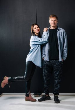 Çift stüdyo ortamında birlikte poz veriyor. İki birey bir stüdyoda, şık bir arka planla gündelik ama şık bir kıyafet sergiliyorlar..