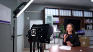 Esmer kadın bir video kaydı için kamerayla konuşuyor. Stüdyoda modern blog yaratıcısı. Bulanık arkaplan.
