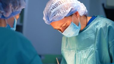 Odaklanmış beyaz kadın cerrah operasyonda metal aletler kullanıyor. Tanınmayan ameliyat hemşiresi ön planda duruyor..