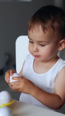 Küçük oğlan oyuncak yumurtalarla oynadığı oyuna odaklanmış. Çocuk masada oturup oyuncakları topluyor ve kutuya geri koyuyor. Dikey video