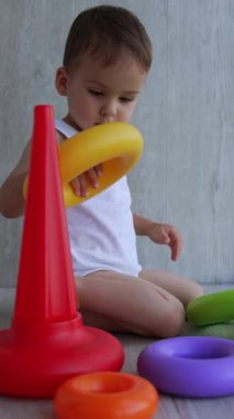 Güzel bebek yerde oyuncaklarla oynuyor. Çocuk oyuncak piramidi yapmakla meşgul. Dikey video