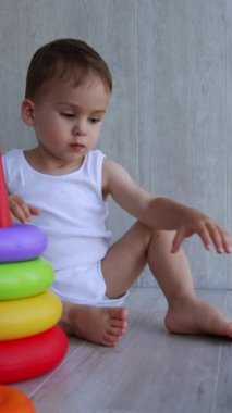 Beyaz şirin bir bebek yerde piramit toplayarak oyun oynuyor. Gülümseyen mutlu çocuk bir oyun ödüyor. Dikey video