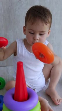 Bir yaşındaki çocuk piramidi kurmakla meşgul. Bebek yüzükleri temel olarak takar ve sonra çıkarır. Yüksek açı. Dikey video