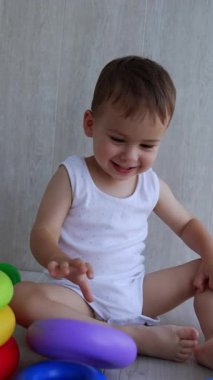 Aktif Kafkas bebek oyuncaklarıyla oynuyor. Bebek çocuk yere oturup oyuncak piramidin yüzüklerini fırlatıyor. Dikey video