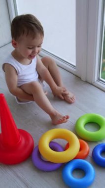 Küçük çocuk bir oyunun yardımıyla renkleri öğreniyor. Sevimli bebek balkonda oyuncak piramitle oynuyor. Üst Manzara. Dikey video