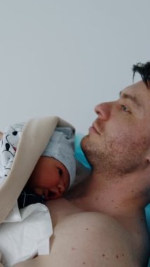 Beyaz bir adam yeni doğmuş bir çocuğu göğsünde tutuyor. Doğum kliniklerinde ten tene konsept. Dikey video