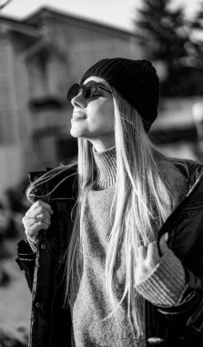 Kız güneşli kış gününün tadını çıkarıyor. Genç bir kadın dışarıda duruyor, güneş ışığında bereli ve ceketli..