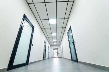 Camdan kapıları olan modern bir koridor. Gösterişli bir koridorda çağdaş mimari tarzında duvarları kaplayan birden fazla cam kapı bulunur..