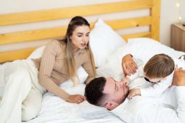 Aile evde neşeli anların tadını çıkarıyor. Bir çift ve küçük çocukları rahat bir yatakta neşeli bir atmosfer yaratarak neşeli etkileşimler yaşarlar..