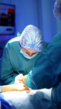 Yaralı elden cerrahi operasyon. Kadın doktor metal aletlerle hastanın üzerine eğilmiş. Dikey video.