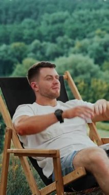 Beyaz tişörtlü mutlu adam laptopuyla işe ara veriyor. Adam ellerini başının arkasına koyar ve bir sandalyede rahatlar. Dikey video
