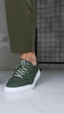Haki kotlu ve spor ayakkabılı bir adam rahat spor ayakkabılarını gösteriyor. Kapatın. Stüdyoda şık ayakkabı sunumu. Dikey video