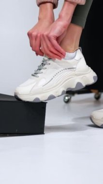 Model, modaya uygun beyaz ayakkabılarını giyiyor. Stüdyoda gösterilen şık ve rahat ayakkabılar. Dikey video