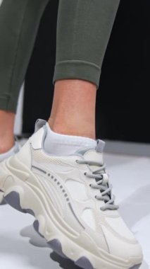 Koyu yeşil taytlı ve beyaz spor ayakkabılı bir bayan. Kapatın. Stüdyo ayakkabıları tanıtımı. Dikey video