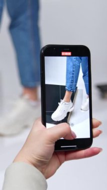 Modern spor ayakkabıları sergileyen bir kızın cep telefonu videosunu çekiyorum. Stüdyoda şık bir görünüm. Dikey video
