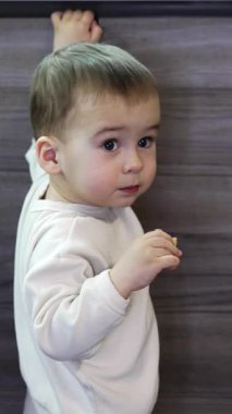 Beyaz kazaklı, melek gibi çocuk mutfak büfesinde duruyor. Gülümseyen çocuk aynı anda hem bir şeyler yiyip hem de kapıları açıyor. Bebek odadan çıkar ve uzaklaşır.