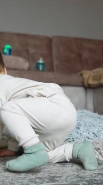 Beyaz takım elbiseli bir bebeğin yerde oturup kurabiye yemesi. Çocuk yemeği yere düşürür, onu geri almak ve yemek için ayağa kalkar..