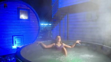 Çekici, rahat, çizgili mayo giymiş beyaz kadın jakuzide oturuyor. Kışın güzellik ve kaplıca prosedürleri.