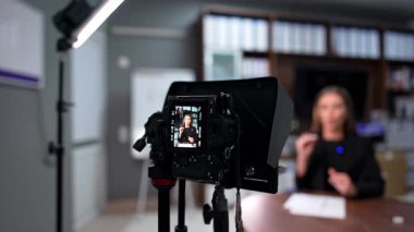 Uzun saçlı, beyaz bir kadın aktif bir şekilde video çekiyor ve el kol hareketi yapıyor. Modern eğitim blogları. Bulanık arkaplan.