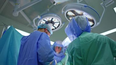 Ameliyat masasında duran mavi cüppeli erkek cerrahların dikiz görüntüsü. Cerrahi ekibinde çalışan doktorlara düşük açılı bakış açısı.