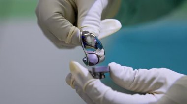 Doktorun lateks eldivenli elleri diz eklemi protezi tutuyor. Ortopedi ve travma cerrahı. Kapat..