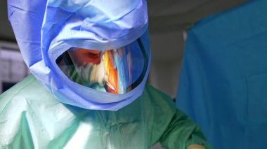Koruyucu kask takan gülümseyen erkek cerrah. Ameliyat, doktorun kaskının ekranına yansıyor..