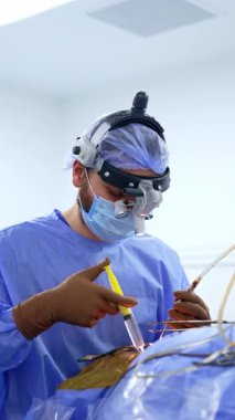 Cerrahi loplardaki sakallı beyaz cerrah şırınganın içine tuz solüsyonu püskürtür. Doktor kan emme aleti uyguluyor. Dikey video.