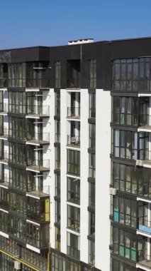 Yeni inşa edilmiş şehir mimarisi. Şehirdeki konut binasının dışında. Uzun cam pencereleri ve balkonları olan modern bir bina. Dikey video