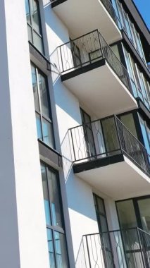 Gökyüzü arkaplanındaki apartman blokları. Pencereleri ve büyük balkonları olan modern bir apartman dairesi. Dikey video